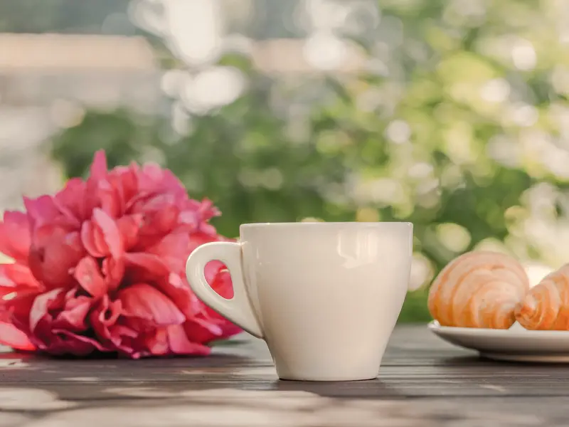A cup of coffee and flowers on a table in the morning